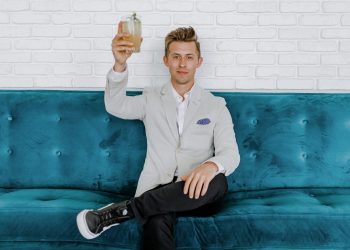 man in gray blazer raising drinking glass while sitting on sofa