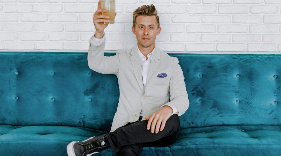 man in gray blazer raising drinking glass while sitting on sofa